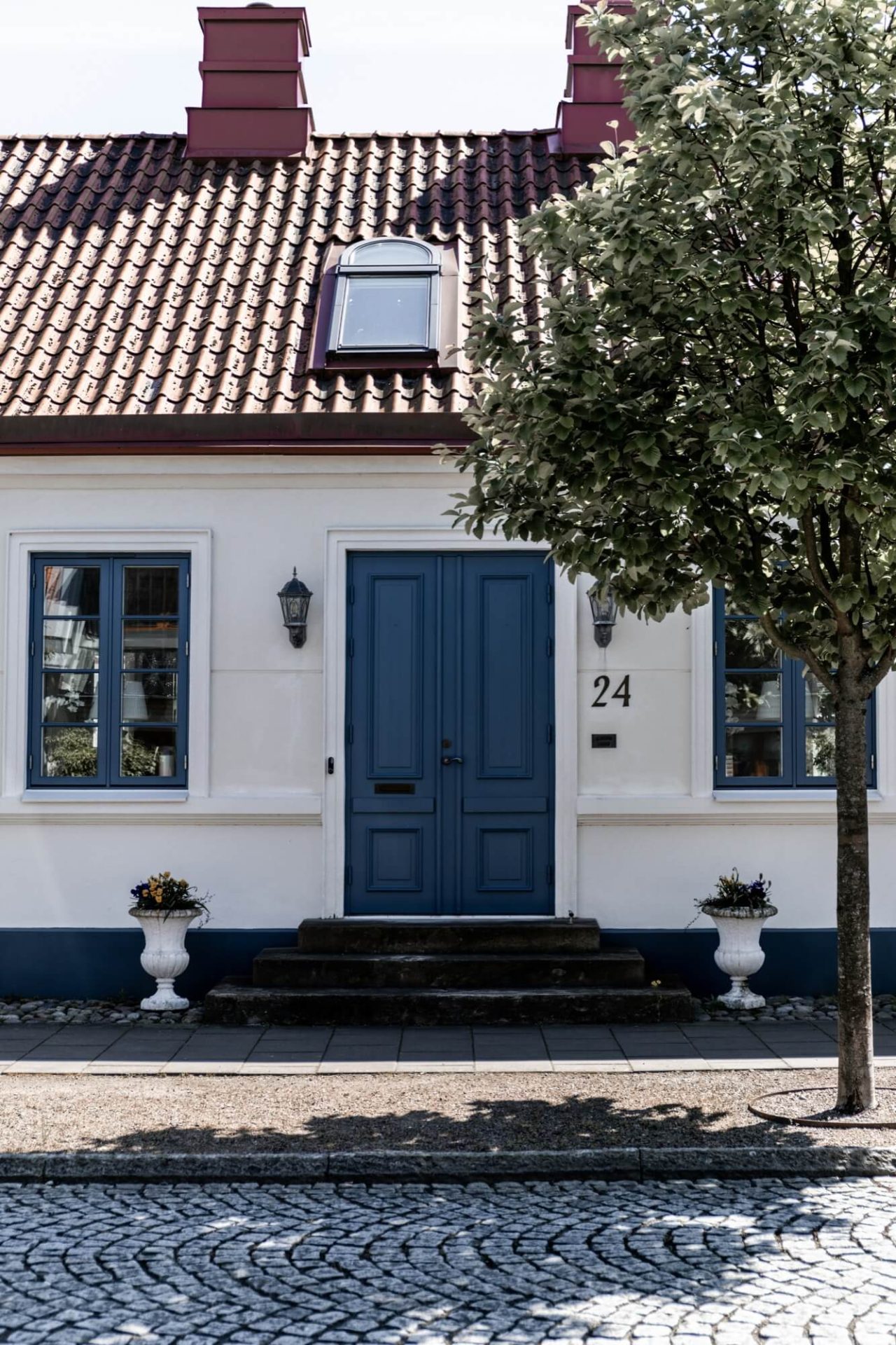 En kullerstensbelagd trottoar leder fram till ett hus med klassisk vit puts, blå dörr och fönster